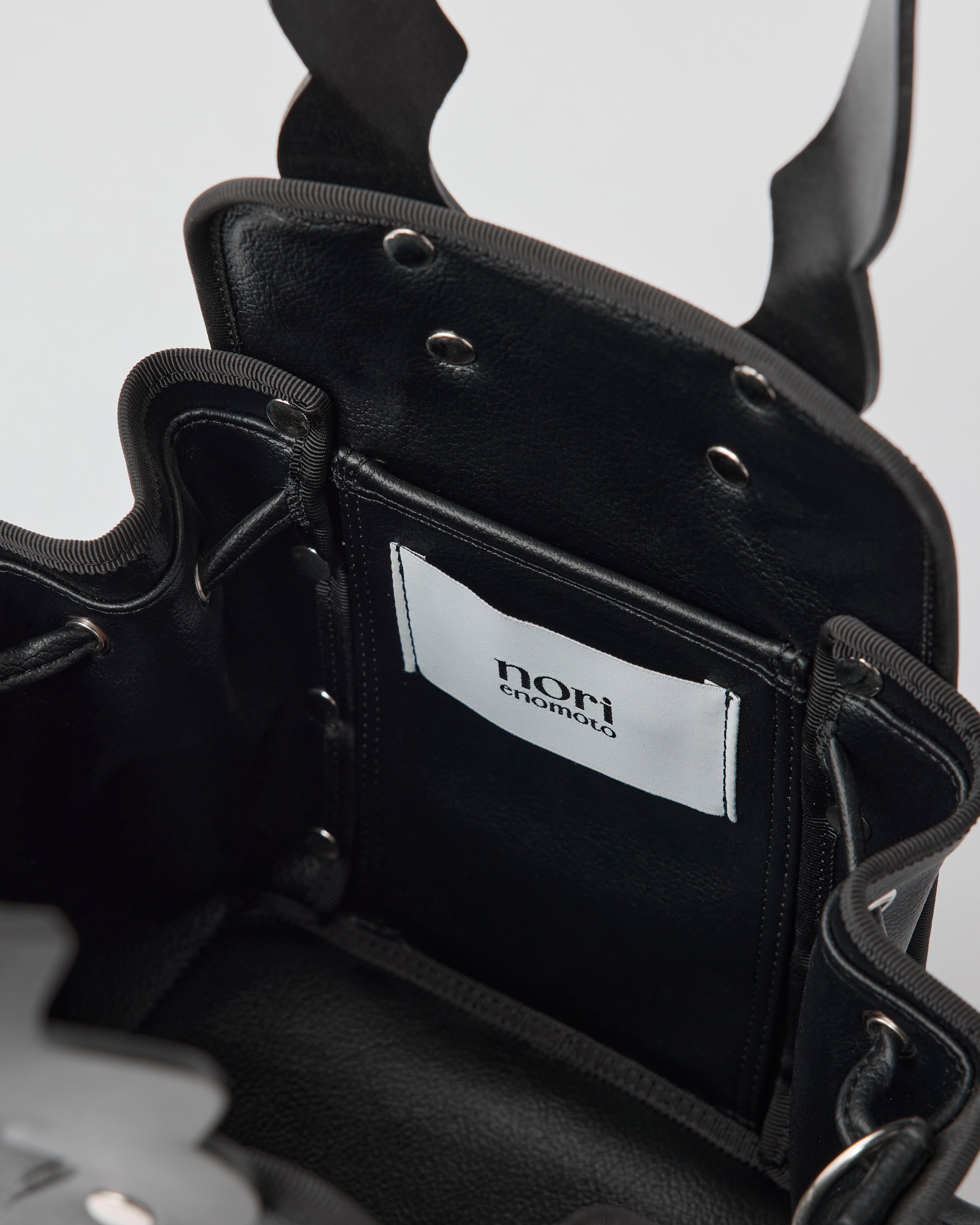 本革ハンドルの巾着型ハンドバッグ。サイドのドローストリングでシルエットを変化可能。500mlペットボトル対応サイズで内ポケット付き。取り外し可能なチェーンストラップでショルダー・クロスボディ両用。