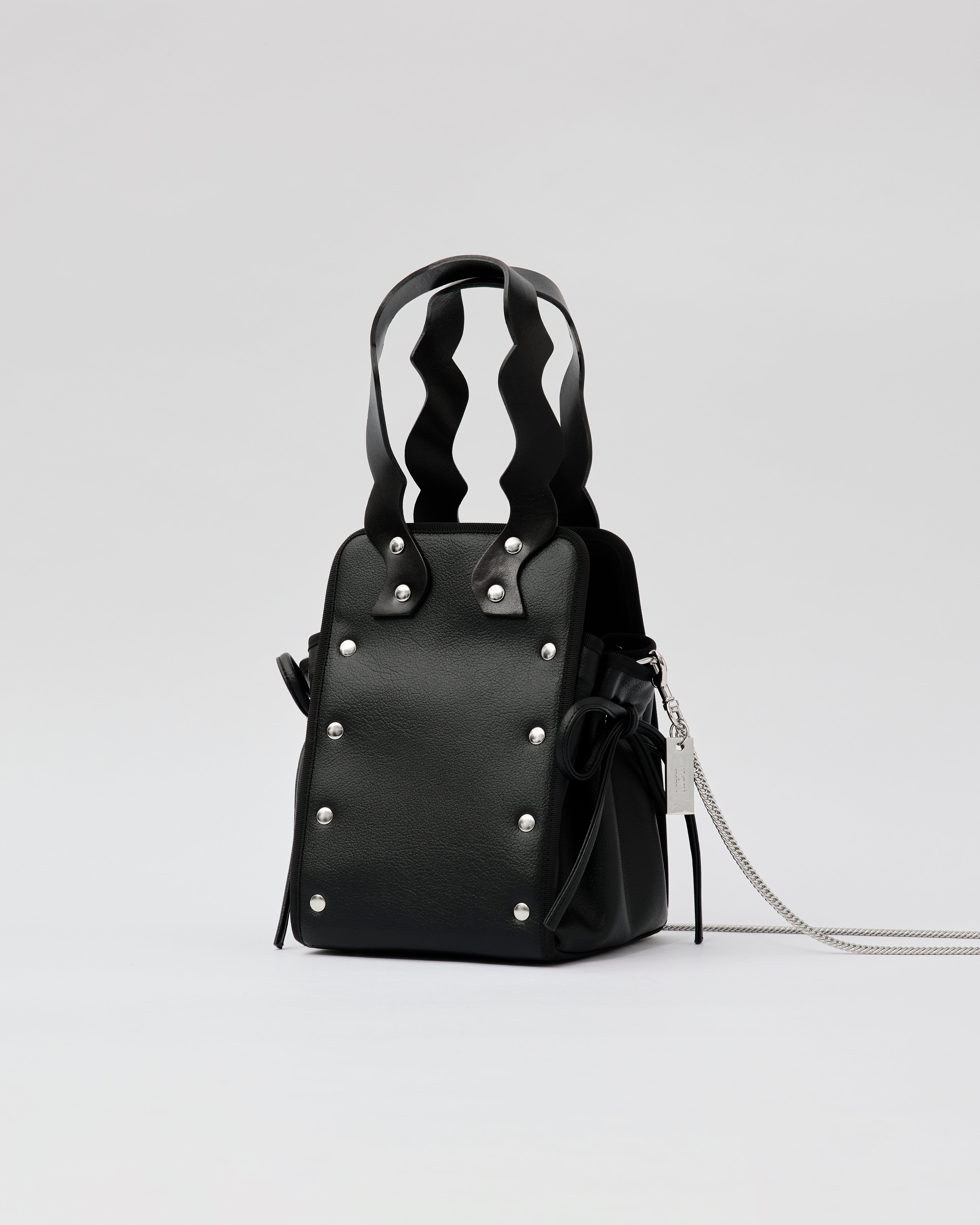 本革ハンドルの巾着型ハンドバッグ。サイドのドローストリングでシルエットを変化可能。500mlペットボトル対応サイズで内ポケット付き。取り外し可能なチェーンストラップでショルダー・クロスボディ両用。