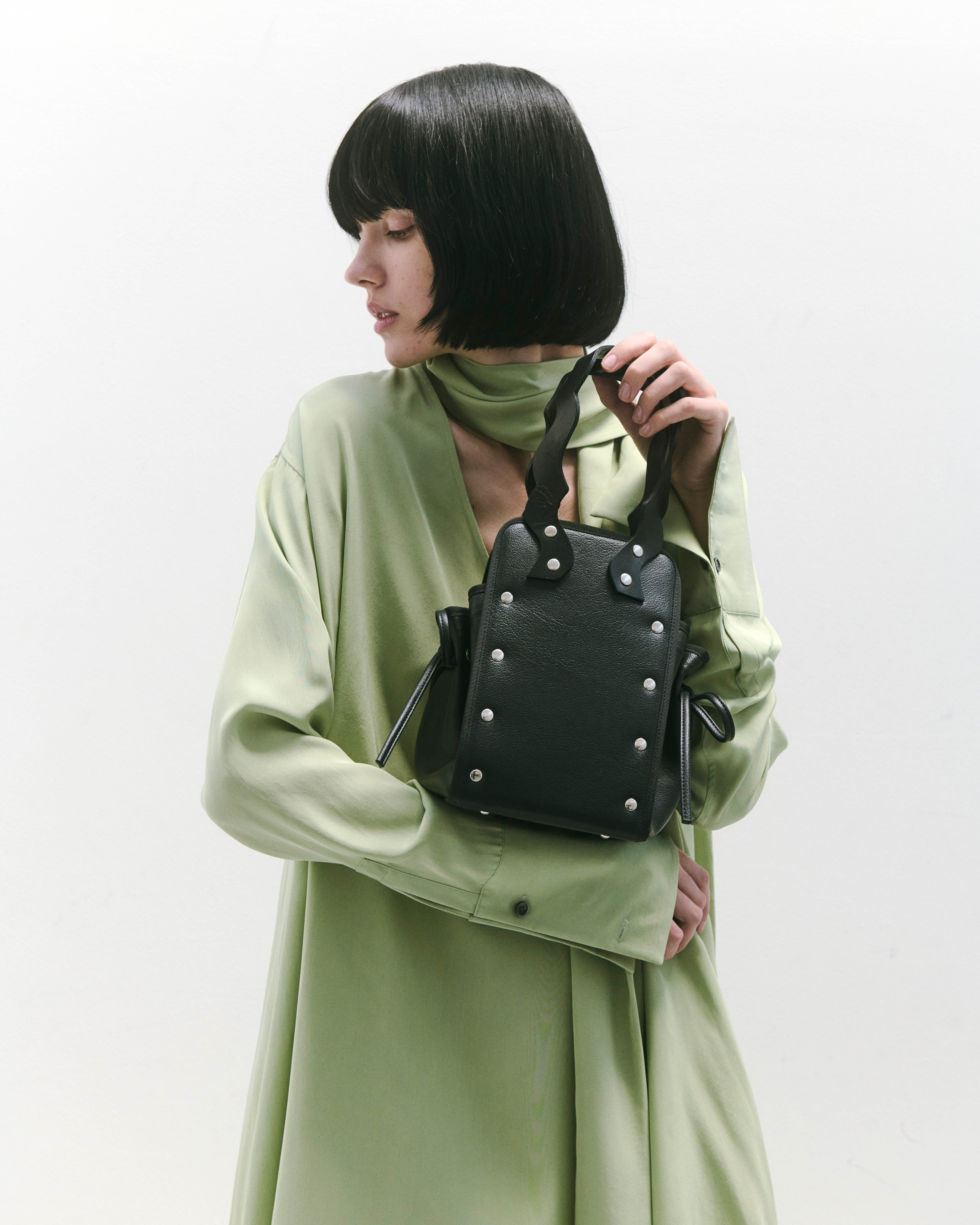 本革ハンドルの巾着型ハンドバッグ。サイドのドローストリングでシルエットを変化可能。500mlペットボトル対応サイズで内ポケット付き。取り外し可能なチェーンストラップでショルダー・クロスボディ両用。