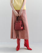 本革ハンドルの巾着型ハンドバッグ。サイドのドローストリングでシルエットを変化可能。500mlペットボトル対応サイズで内ポケット付き。取り外し可能なチェーンストラップでショルダー・クロスボディ両用。