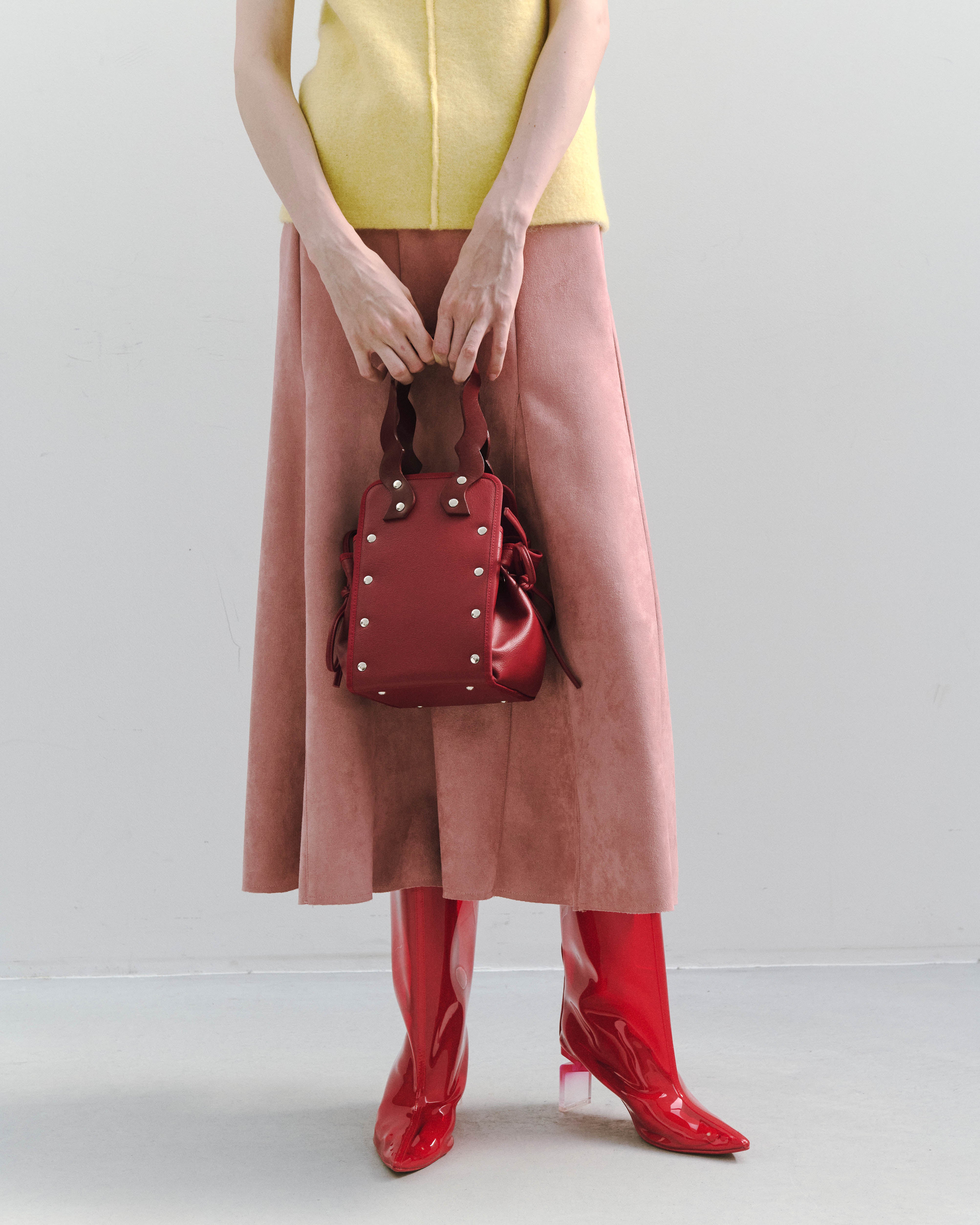 本革ハンドルの巾着型ハンドバッグ。サイドのドローストリングでシルエットを変化可能。500mlペットボトル対応サイズで内ポケット付き。取り外し可能なチェーンストラップでショルダー・クロスボディ両用。