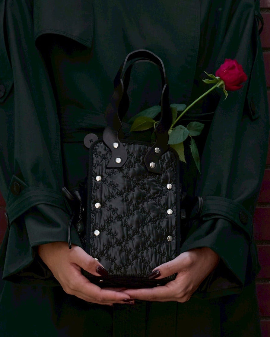 本革ハンドルの巾着型ハンドバッグ。サイドのドローストリングでシルエットを変化可能。500mlペットボトル対応サイズで内ポケット付き。取り外し可能なチェーンストラップでショルダー・クロスボディ両用。