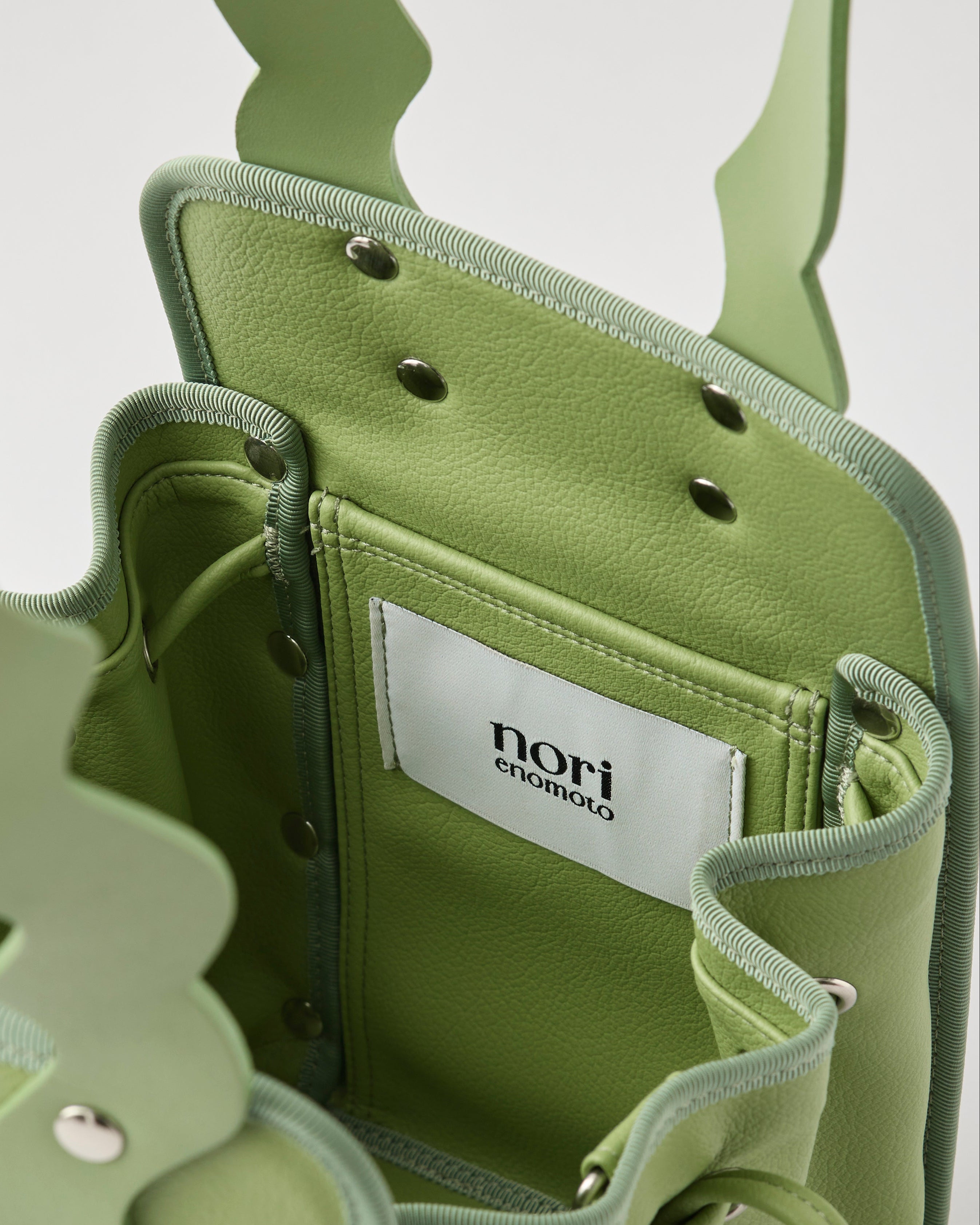 本革ハンドルの巾着型ハンドバッグ。サイドのドローストリングでシルエットを変化可能。500mlペットボトル対応サイズで内ポケット付き。取り外し可能なチェーンストラップでショルダー・クロスボディ両用。