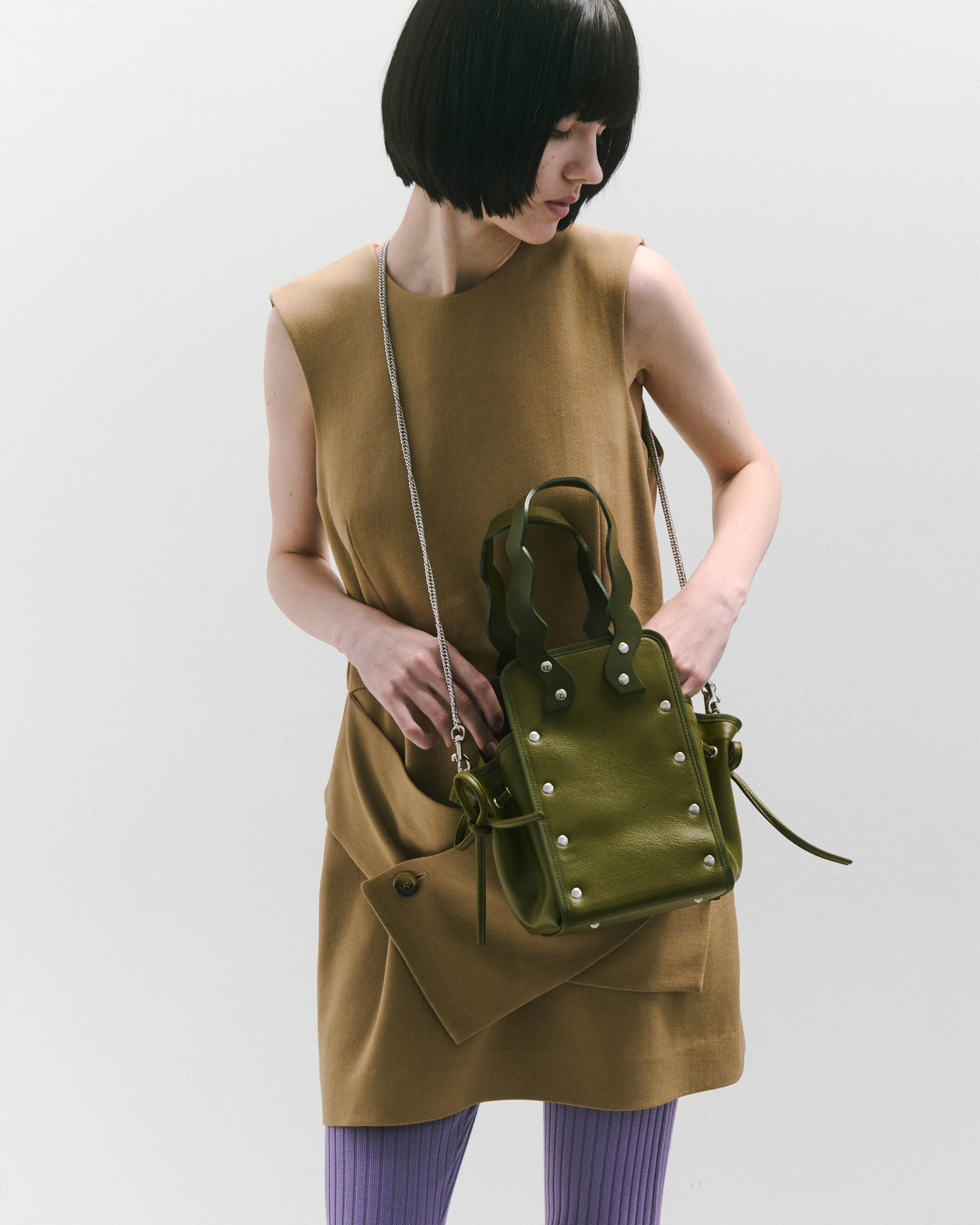 本革ハンドルの巾着型ハンドバッグ。サイドのドローストリングでシルエットを変化可能。500mlペットボトル対応サイズで内ポケット付き。取り外し可能なチェーンストラップでショルダー・クロスボディ両用。