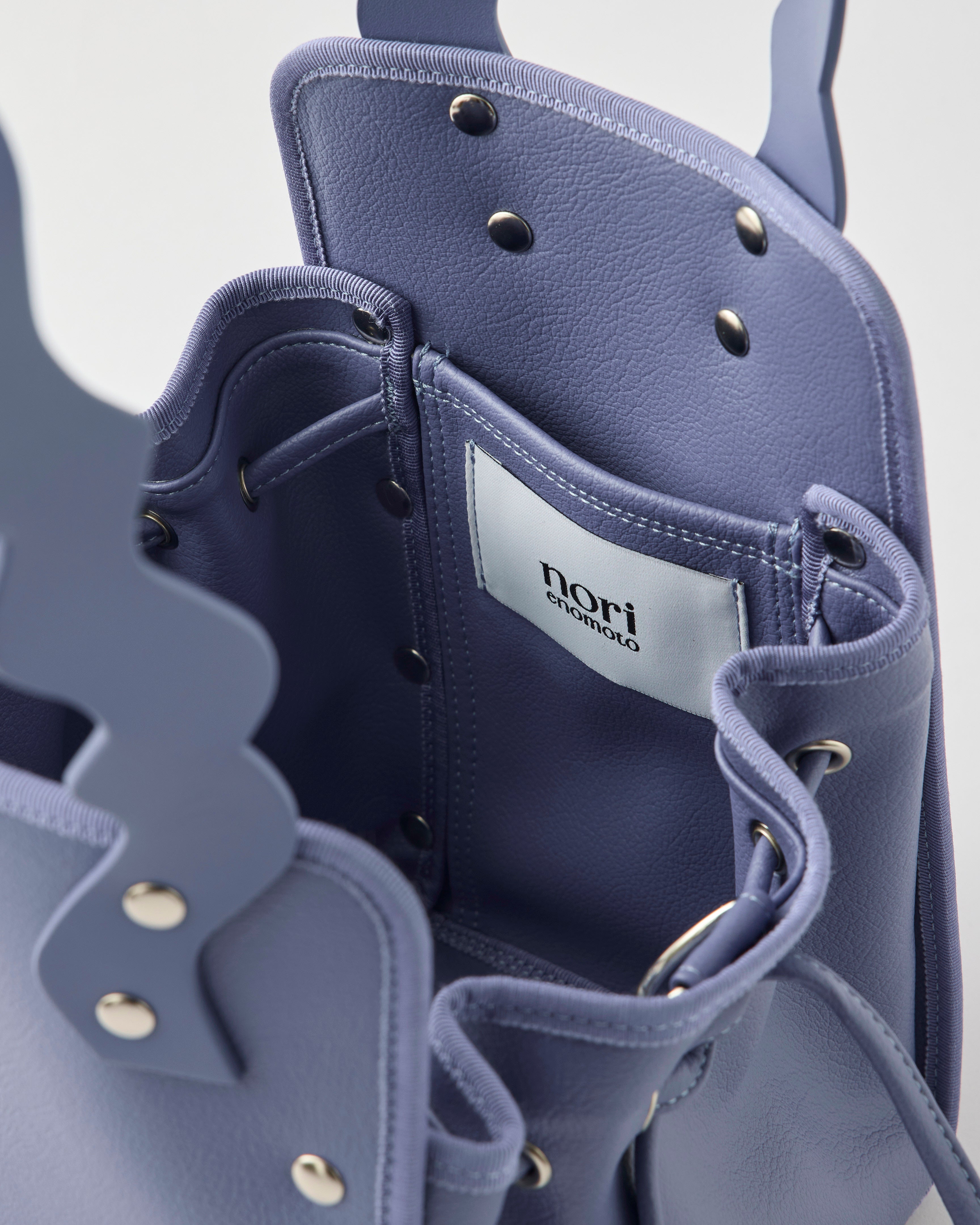 本革ハンドルの巾着型ハンドバッグ。サイドのドローストリングでシルエットを変化可能。500mlペットボトル対応サイズで内ポケット付き。取り外し可能なチェーンストラップでショルダー・クロスボディ両用。