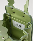 本革ハンドルの巾着型ハンドバッグ。サイドのドローストリングでシルエットを変化可能。500mlペットボトル対応サイズで内ポケット付き。取り外し可能なチェーンストラップでショルダー・クロスボディ両用。